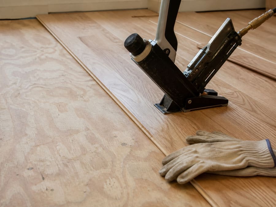 New oak boards being laid across a prepared subfloor in a bright empty room